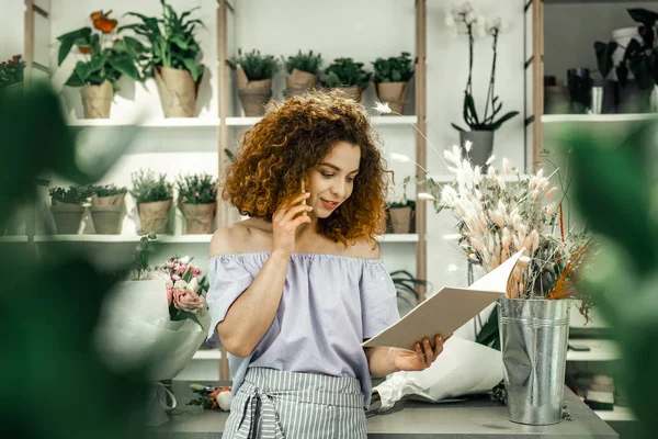 Travailleur bouclé de la boutique florale regardant dans le carnet et appelant le client — Photo