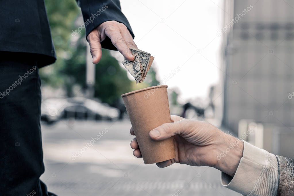 Rich business man stopping on street and compassionately sharing money