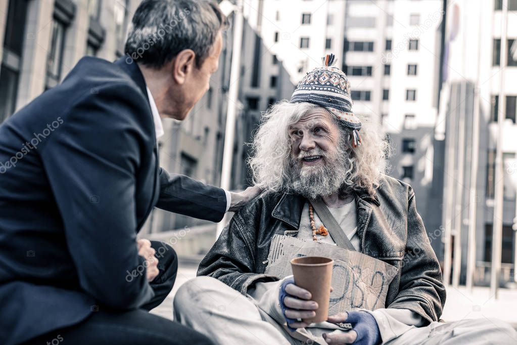 Smiling happy long-haired homeless man taking money from kind businessman