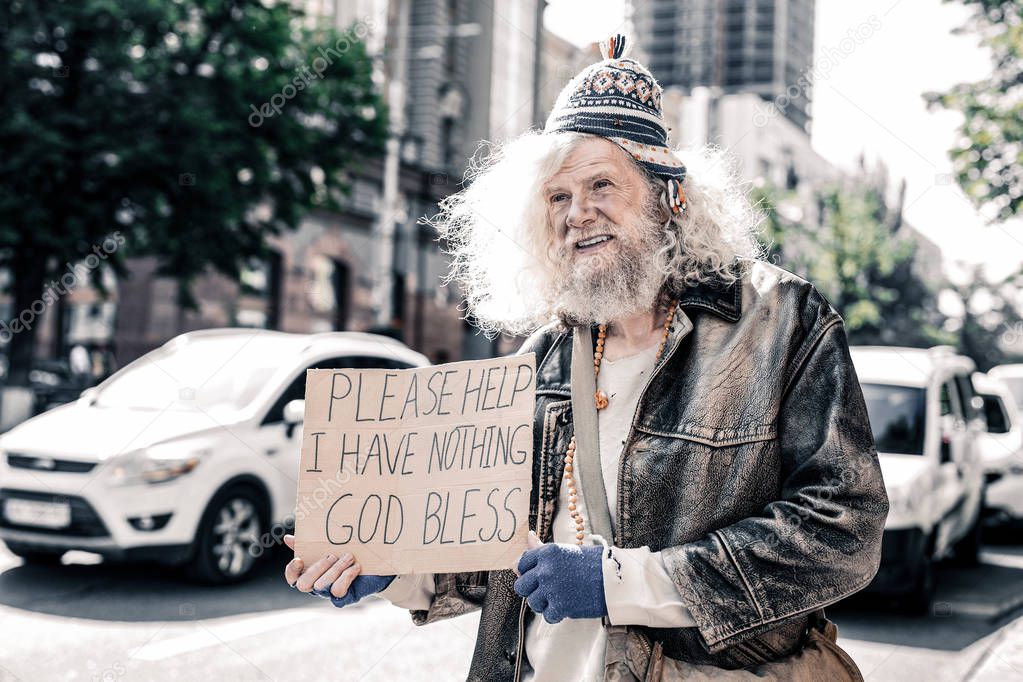 Miserable dirty old man being poor homeless and standing with cardboard