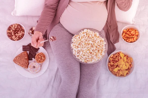 Szőke szép terhes nő kényelmes ruhát enni snack — Stock Fotó