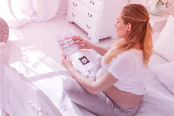 Jovem mulher grávida de cabelos longos em uma camiseta branca olhando para o calendário — Fotografia de Stock