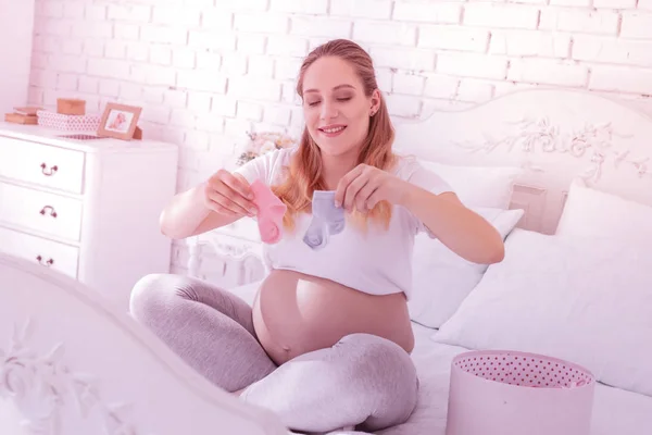 Μακρυμάλλης έγκυος γυναίκα σε ένα λευκό t-shirt που κατέχουν μικρές κάλτσες — Φωτογραφία Αρχείου