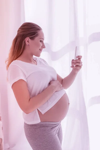 Genç ışınlama uzun saçlı hamile kadın beyaz bir t-shirt yapımı selfie — Stok fotoğraf