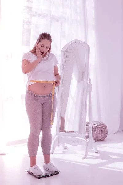 Joven mujer embarazada radiante de pelo largo con una camiseta blanca que se ve asombrada — Foto de Stock