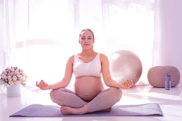 Young beaming long-haired pregnant woman in a white t-shirt meditating — Stock Photo, Image