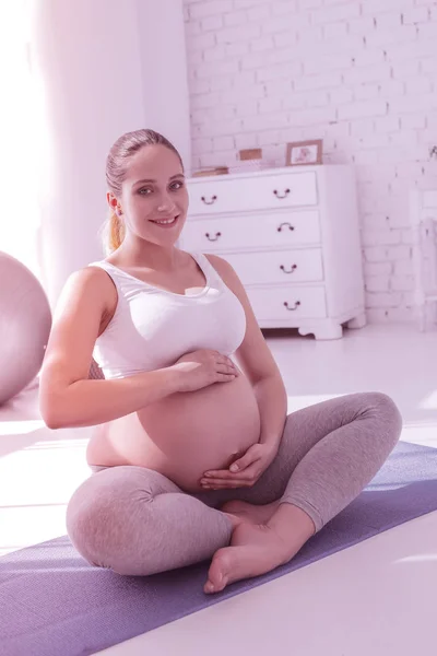 Молодая сияющая длинноволосая беременная женщина в белой футболке чувствует себя великолепно — стоковое фото
