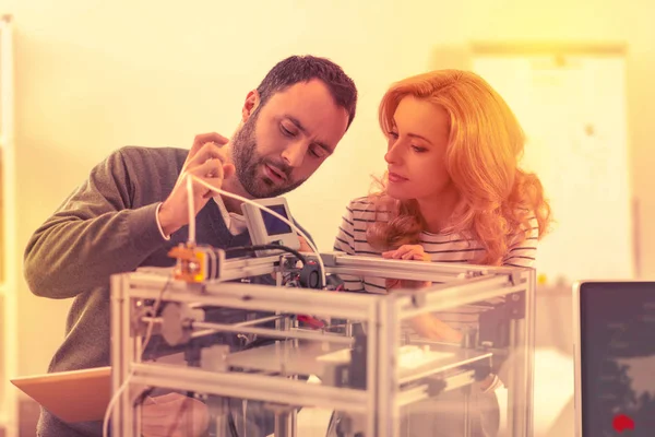 Hombre y mujer serios jugando con el mecanismo de una impresora 3D a estrenar . — Foto de Stock