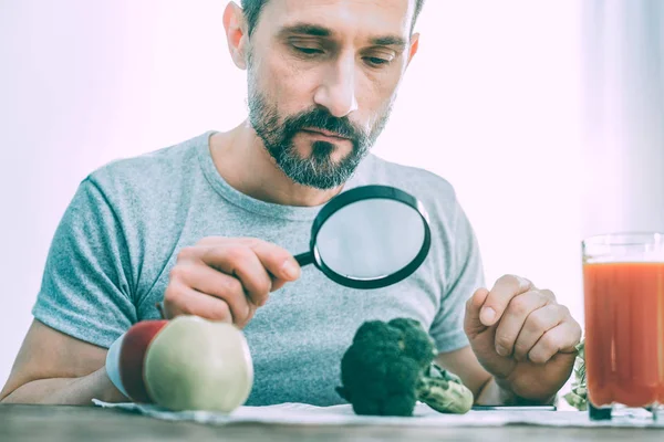 Hombre tranquilo indiferente estudiando diferentes tipos de verduras — Foto de Stock