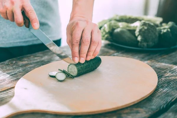 Homem cortando pepinos para fazer uma salada saborosa saudável — Fotografia de Stock