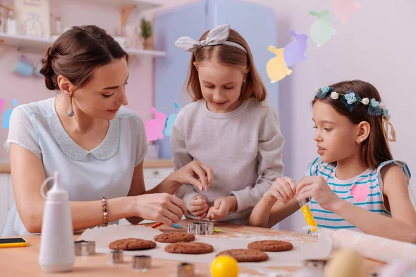 Задоволені дівчата допомагають своїй мамі пекти печиво — стокове фото