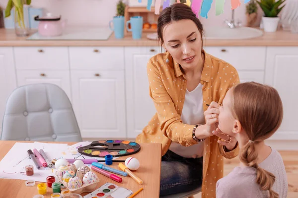 Geconcentreerd brunette vrouw schilderij gezicht van haar jongen — Stockfoto