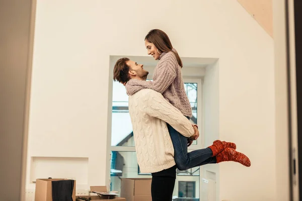 Loving dark-haired husband lifting his appealing wife in new room — Stock Photo, Image