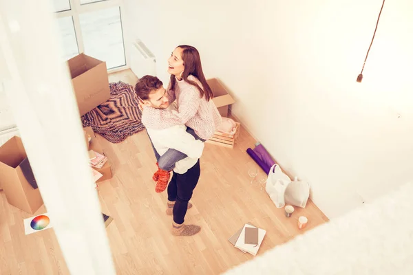 Fru skrattar medan hennes man lyfta hennes stående i sitt nya rum — Stockfoto