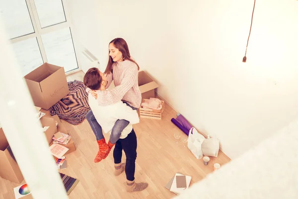 Strong dark-haired man wearing white sweater lifting his lovely girl — Stock Photo, Image