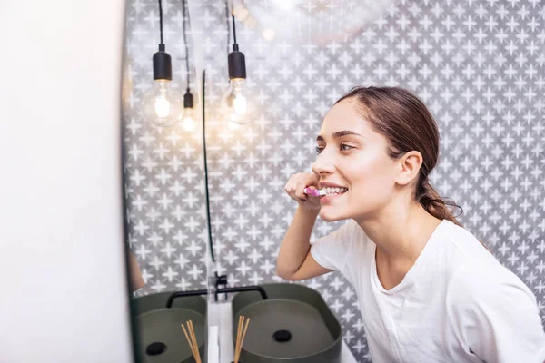 Mulher de cabelos escuros escovando os dentes em seu banheiro moderno luz — Fotografia de Stock