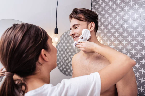 Precioso marido mirando a la esposa poniendo espuma de afeitar en su cara — Foto de Stock