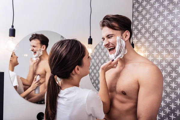 Муж смеётся, когда его жена наносит ему на лицо пену для бритья. — стоковое фото
