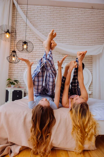 Hermanas con el pelo largo y rubio levantando las piernas mientras se estiran en la cama — Foto de Stock