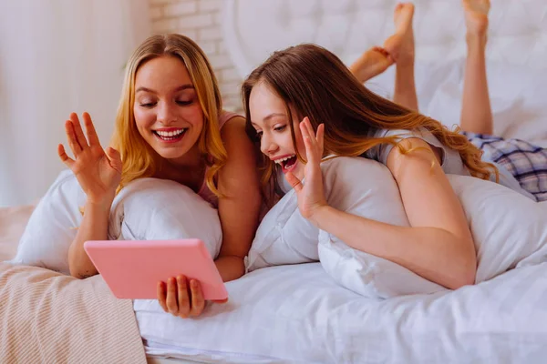 Loving sisters chilling in bed and having video chat with parents