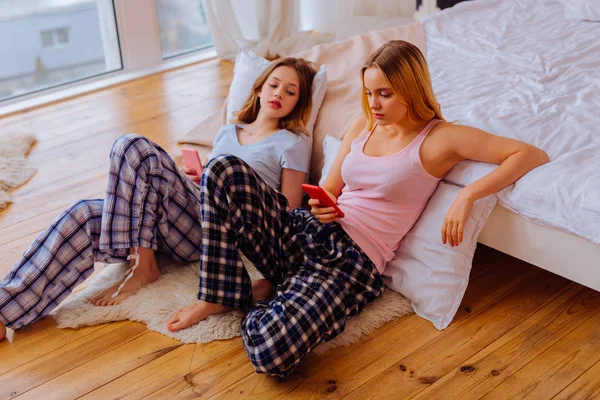 Дві сестри використовують свої смартфони, сидячи на підлозі біля ліжка — стокове фото