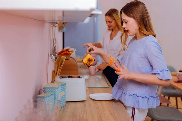 Teenage sister wearing blue blouse touching hot toast in the morning