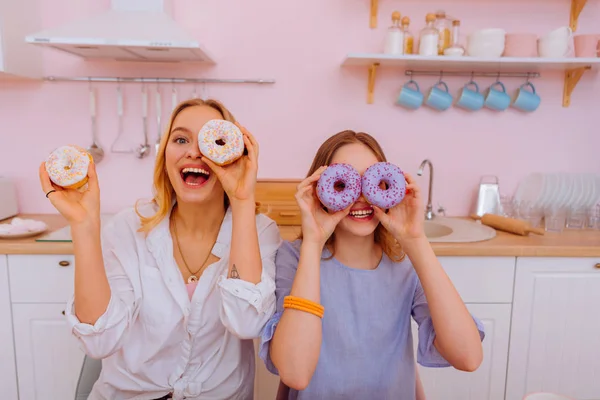 Hermanas divirtiéndose mostrando donas dulces en la cocina — Foto de Stock