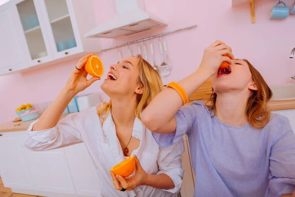 Funny sisters squeezing orange juice into mouths during breakfast — Stock Photo, Image