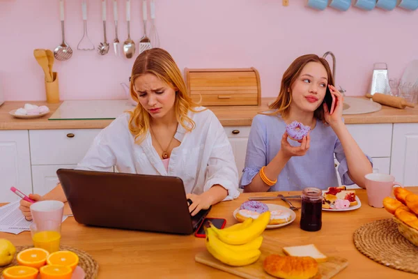 Adolescente hermano hablando por teléfono y comiendo cerca de la hermana trabajadora — Foto de Stock