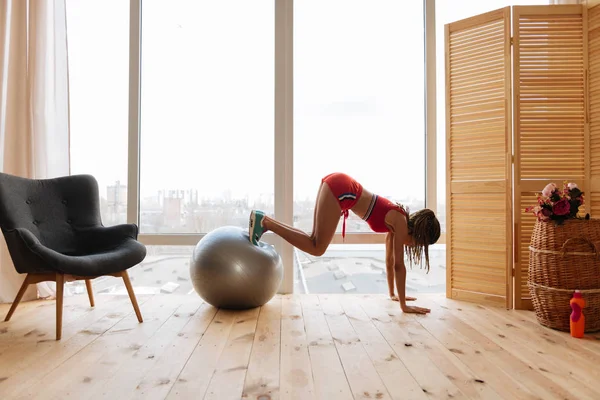 Slim active woman exercising on fitness ball in the morning