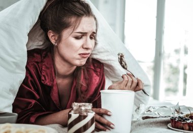 Depressed woman eating a lot of sweets clipart