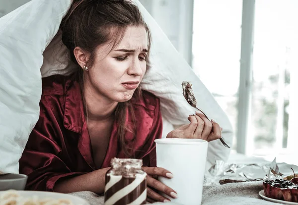 たくさんのお菓子を食べる憂うつな女性 — ストック写真