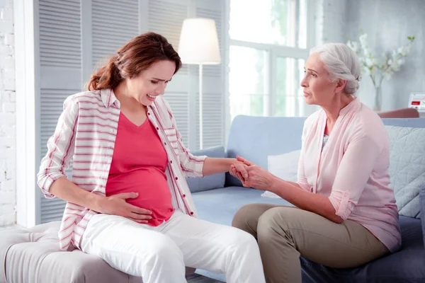 Grey-haired woman holding hand of her pregnant daughter — Stock Photo, Image