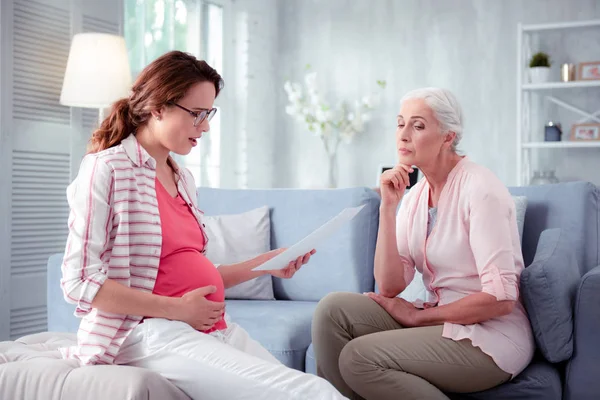 Mother listening to pregnant daughter reading prescription of doctor — Stock Photo, Image
