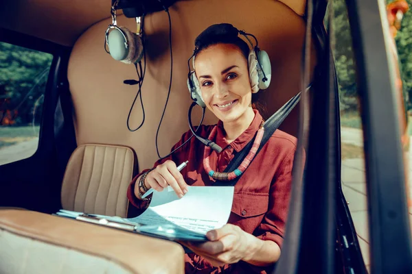 Uśmiechnięta atrakcyjna dama w czerwonej koszulce sprawdzająca swoje papiery podczas lotu — Zdjęcie stockowe
