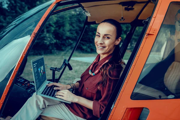 Señora adulta positiva con amplia sonrisa sentada en helicóptero con portátil — Foto de Stock