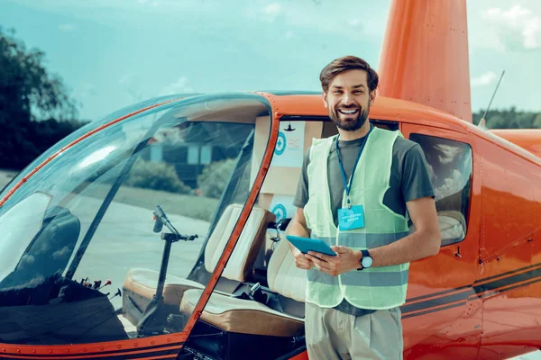 Glad mörkhårig volontär med brett leende står nära helikopter — Stockfoto
