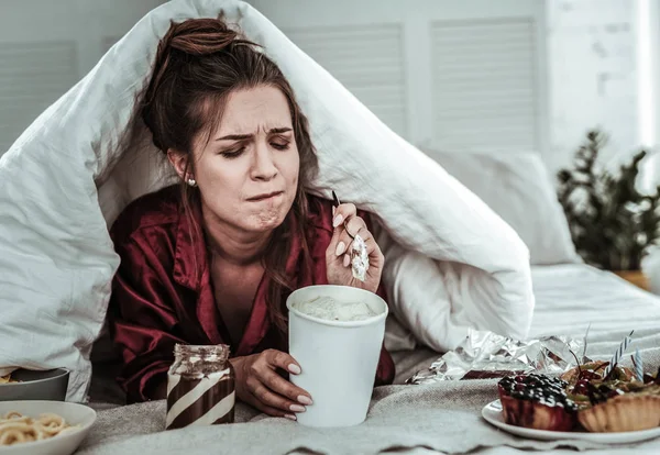 Стрессовая женщина, покрытая одеялом, поедающая сладости — стоковое фото