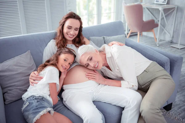Pregnant woman sitting on sofa between daughter and mother — Stok fotoğraf