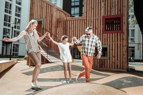 Encantada menina positiva se divertindo com seus pais — Fotografia de Stock