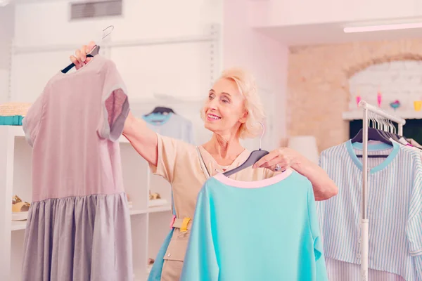 Женщина средних лет выбирает одно из двух платьев в бутике — стоковое фото