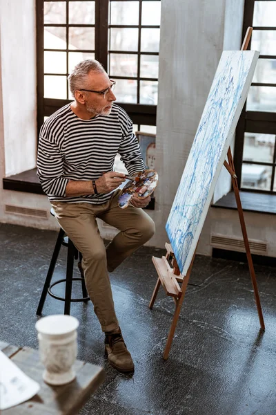 Artist wearing beige trousers and striped shirt working on new canvas — Stock Photo, Image