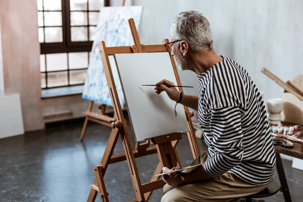 Artiste assis sur une chaise près du chevalet de peinture tout en travaillant — Photo