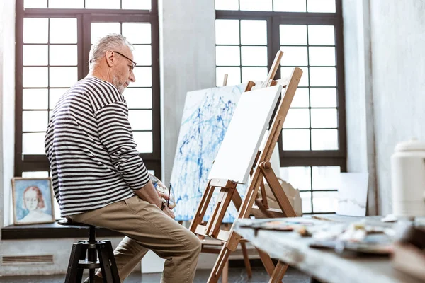 Bearded artist looking at white canvas and having creative ideas — Stock Photo, Image
