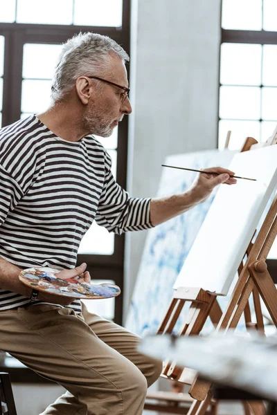 Καλλιτέχνης κρατώντας βούρτσα ζωγραφικής στο αριστερό χέρι ενώ ζωγραφική τοπίο — Φωτογραφία Αρχείου