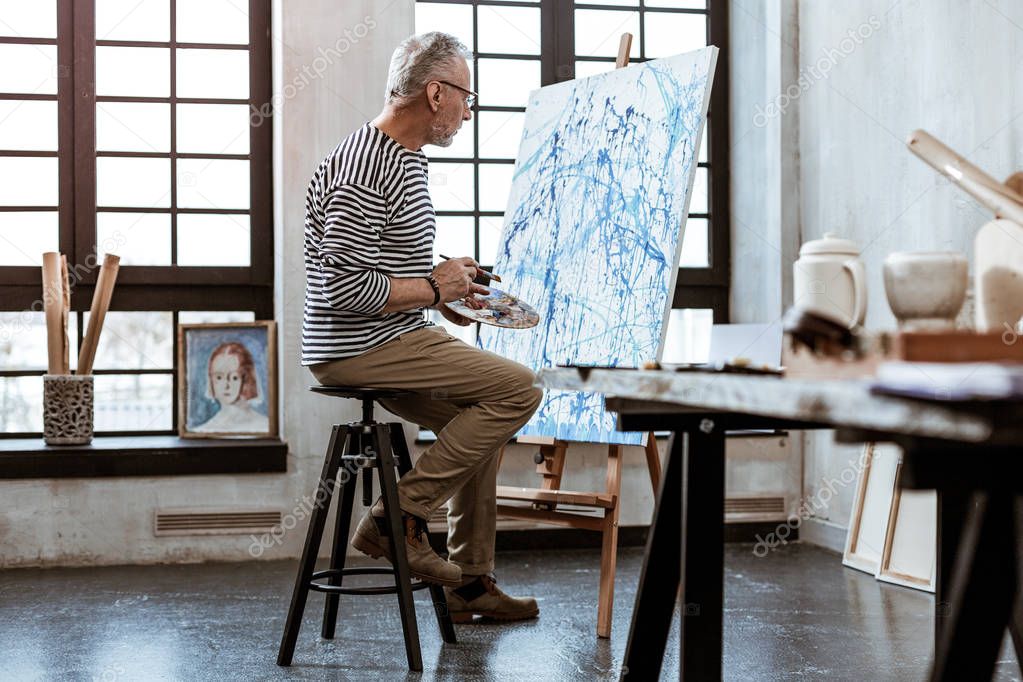 Experienced grey-haired artist working on his new masterpiece
