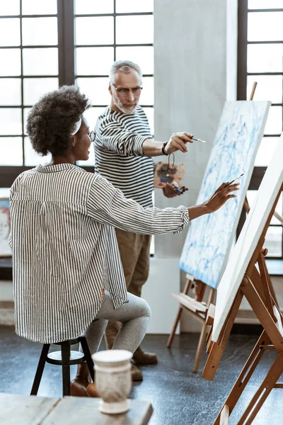 Young art student feeling happy while painting with famous artist — Stock Photo, Image