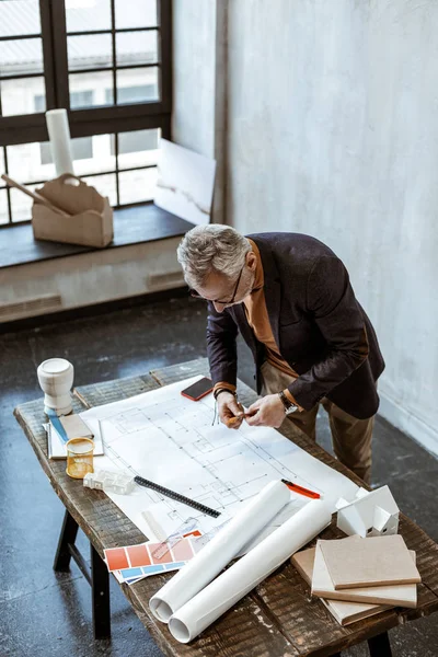 Gråhåriga inrednings arkitekt gör några anteckningar på skisserna — Stockfoto