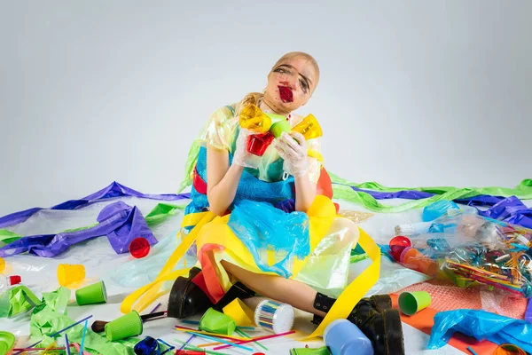 Модель в пластиковой одежде, сидящая на полу в окружении пластикового мусора — стоковое фото