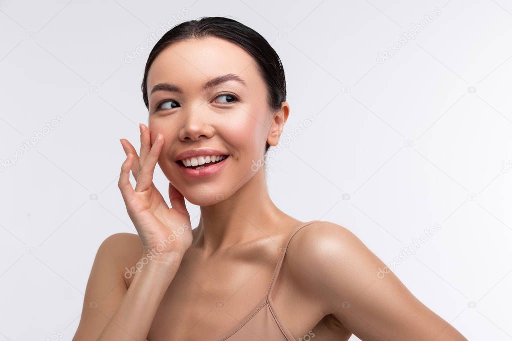Appealing woman with open shoulders touching her beautiful face